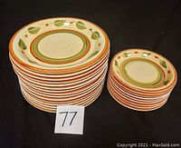Stack of 24 ceramic plates: 15 larger 10-inch plates and 9 smaller 7.5-inch plates, both with orange and green leaf decoration on cream background.
