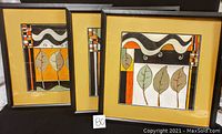 Set of three framed paintings with abstract leaf motifs in black, orange, yellow, and white colors.