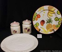 Photo showing all four items: one fruit-themed platter, one white turkey platter, and two floral ceramic canisters with pink lids.