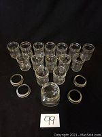 15 clear glass mason jars arranged in rows with 4 metal screw-on rings and 4 metal lids visible in front, shown on a black background.