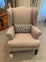 Front view of beige upholstered wing back chair with a zebra pattern rectangular pillow.