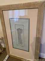 Framed silver-toned artwork showing figure in robe in silver textured frame with matting.