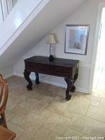 Full view of antique wooden writing desk showing overall size and shape under a staircase.