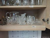 Shelf of glass and china items showing pitchers, sugar bowls, bowls, mugs, and jug as part of the lot