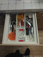 Kitchen utensil drawer with assorted peelers, slicers, graters, egg slicer, hand mixer, and silicone trivet.
