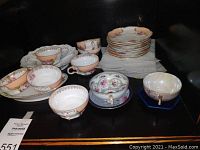 Multiple Austrian china teacups, saucers, and plates arranged on black surface including stacked saucers and a serving plate at back