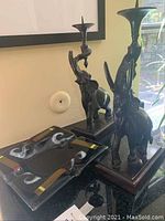 Overall view of two metal elephant candelabra and black glass ashtray on tabletop