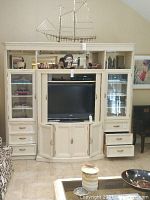 Front full view of large cream entertainment center with central TV space, glass door cabinets on both sides, multiple drawers, and shelves.