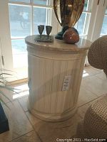 Front view of round storage end table with travertine top, decorative carved band, closed door, brass handle.