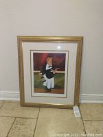 Photo of the entire framed print leaning against a wall, showing the gold ornate frame, and the art depicting a waiter holding a bottle of wine and bowl.