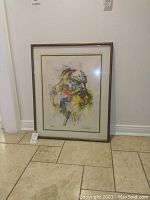 Framed abstract artwork leaning against wall on tile floor.