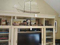 Photo of a metal sailboat sculpture, a tribal mask with facial details, and a few woven baskets on a cream shelving unit.