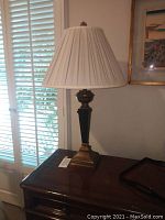 Full view of the table lamp on a wooden surface near window blinds, showing the size and shape of the lamp and lampshade.