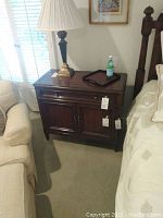 Photo showing the front and side view of the dark stained solid wood nightstand between a bed and chair.
