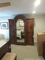 Front view of large wooden wardrobe with central arched mirror and two side doors, showing burl wood pattern.