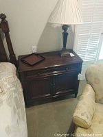 Nightstand shown between bed and armchair with lamp and tray on top