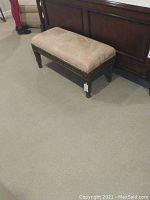 Upholstered bench placed beside a wooden bed frame showing size and condition.