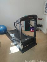 Treadmill on protective mat with exercise ball and fitness steps in background