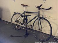 Side profile of Origin 8 single-speed bicycle with drop handlebars and brown saddle mounted on a stand; pump on floor