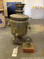 Metal water spout with handles, spout tap, and signs of wear and dirt on the floor surface.