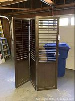 Photo of brown wooden folding room partition showing three hinged panels with horizontal slats and solid bottom panels.