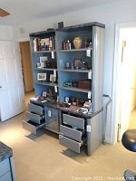 Front view of office cabinet and hutch showing multiple open shelves, drawers, and cabinet doors with frosted glass panels. Items on shelves include books, decorative vases, and various small objects.
