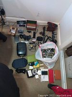 Overview of lot on carpet floor, showing camera, binoculars, monopod, dominoes box, calculator, electronic cables, and devices.