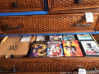 Photo of the top wicker drawer opened showing a variety of DVDs and DVD cases including titles like The Addams Family and others.