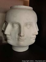 Front and side view of the ceramic vase displaying four human faces merging into one cylindrical form.