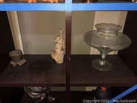 Photo showing a small brown ceramic boot figurine, squirrel figurine, and a clear glass pedestal vase on a wooden shelf section.