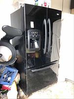 Front view of black Maytag French-door refrigerator showing double doors, ice and water dispenser, and bottom freezer drawer
