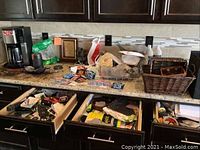 Full view of kitchen countertop with Hamilton Beach coffee maker, miscellaneous items, and two open drawers with assorted kitchen contents