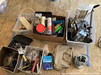Overall view of various boxes and containers filled with different tools and hardware items arranged on floor.