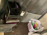Full view of metal cart with black baskets and towels, plastic laundry basket with supplies, and mats on floor.