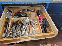 Drawer with flatware including knives, forks, spoons, scissors, and a metal strainer