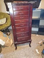 Front view of dark wood jewelry chest with seven drawers and a door with a tag indicating size and description.