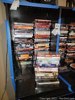 Wide view of a black shelving unit filled with stacks of assorted DVD movies in cases.