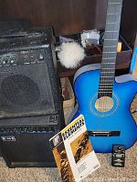 Photo showing the blue acoustic guitar, two amplifiers (Silvertone Smart 1S on top and RMS below), and a music book titled 'Essential Elements for Band'.
