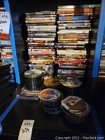 Photo showing multiple stacks of DVDs including titles Wanted, Angels & Demons, Creed, Forrest Gump, and multiple unlabeled DVDs in stacks.