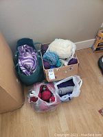 Overview of all four yarn bags and the cardboard box containing yarn in various colors and types on a wooden floor.