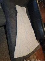 Full view of off white strapless wedding dress laid flat on a couch, showing bodice to hem with textured fabric.