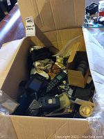 Photo of box containing various electronic items like cell phone, remotes, adapters, earphones, and coins.