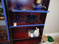 Wide shot of the shelf showing the blue glass decanter, six aperitif glasses, and decorative bowl on stand.
