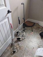 Four foldable carts seen grouped in a corner on tiled flooring against a door and wall, showing hand carts and luggage carts in various heights and designs