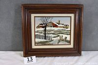 Front view of the framed painting showing a snowy countryside barn scene with wooden brown frame.