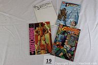 Four DC comic books laid out on a white surface, front covers clearly visible showing the titles and artwork of Watchmen, Superman, and Robin comics.