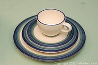 Close-up photo of one set of a cup, salad plate, and dinner plate with blue rings on cream stoneware.