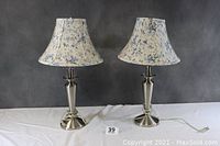 Full view of two matching table lamps with silver bases and blue floral shades against a dark background.