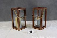 Pair of wooden and glass garden lanterns shown upright with handles visible, placed on a flat surface