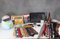 Wide view displaying all items on a table including ties, hats, suspenders, wallet, grooming kit, briefcase, shoeshine kit, wine decanter, business card holder, letter opener, and inflatable globe.